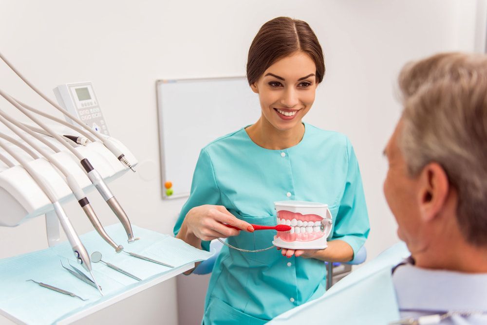 A Female Dentist Is Teaching A Man How To Brush His Teeth — Highlands Denture Clinic in Bowral, NSW