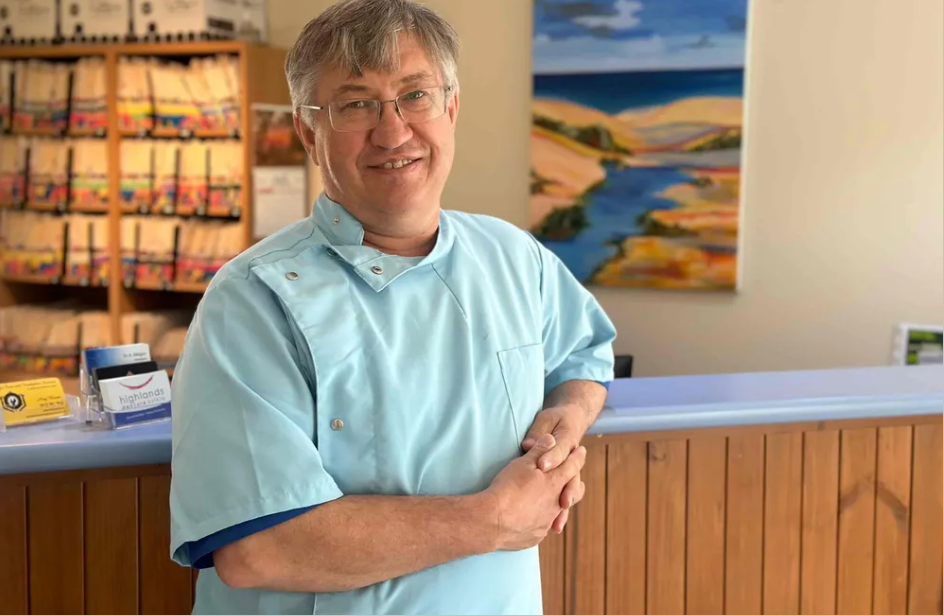 A Dentist Smiles To The Camera In A Reception Area — Highlands Denture Clinic in Willow Vale, NSW
