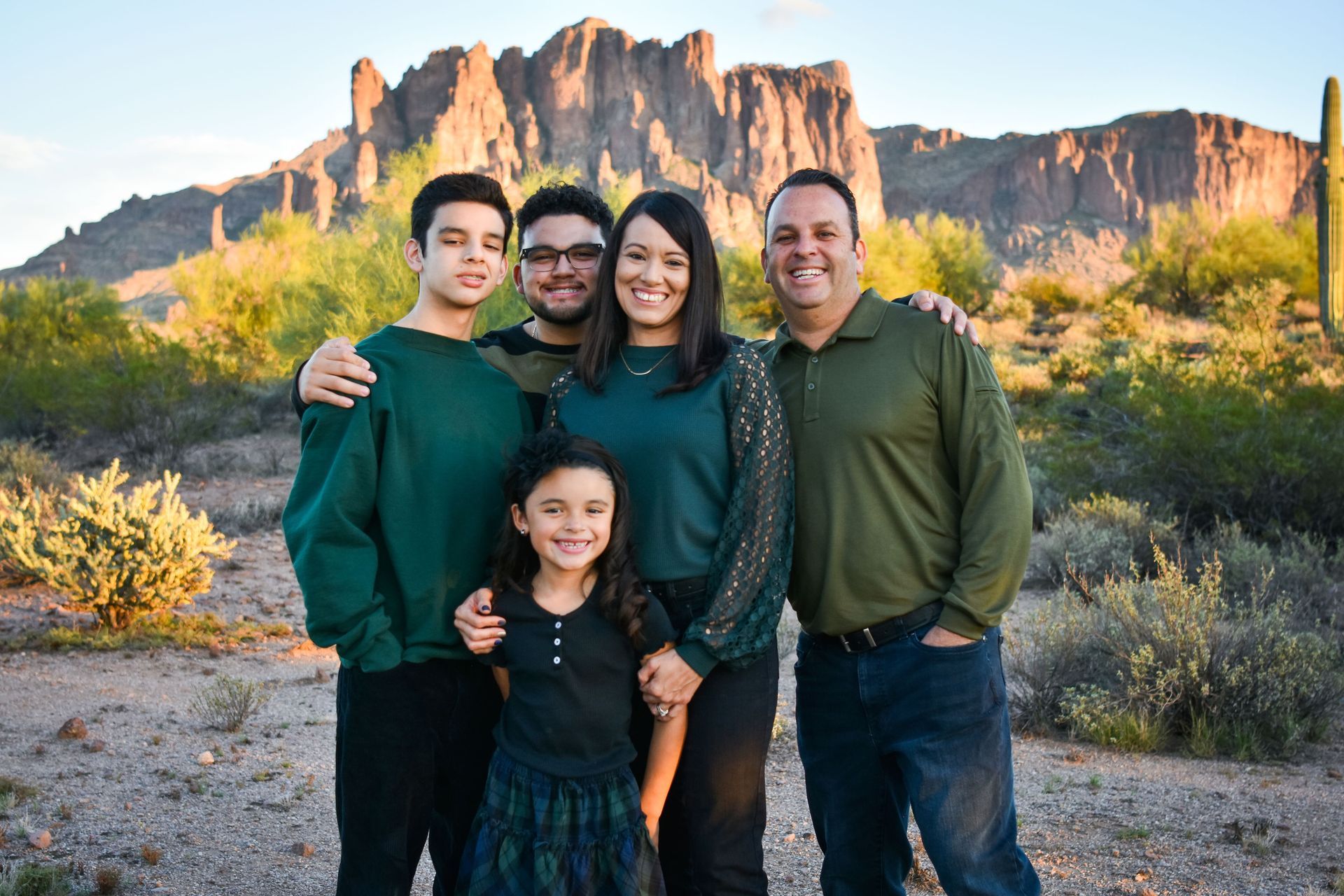 A family is posing for a picture in the desert in front of a mountain.