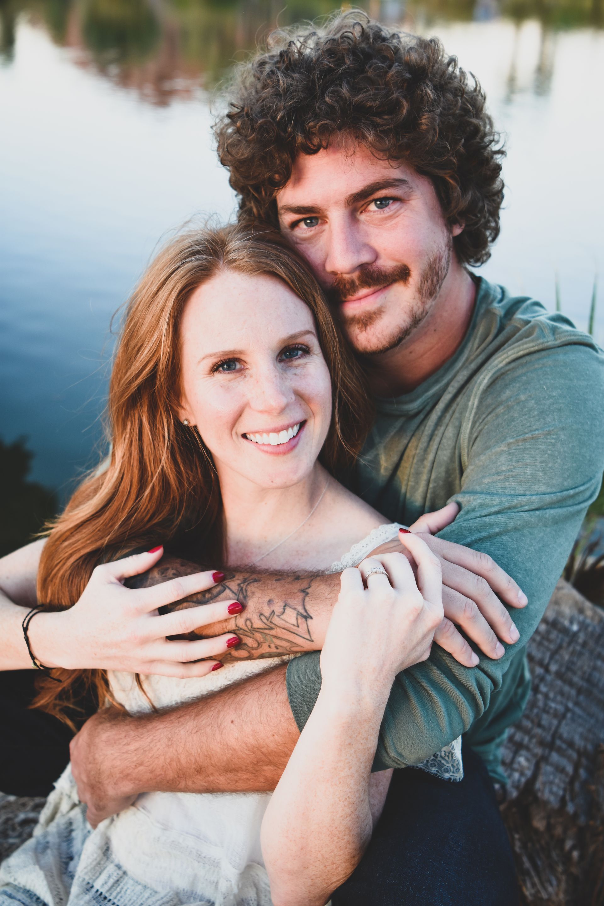 A man and a woman are hugging each other in front of a lake.