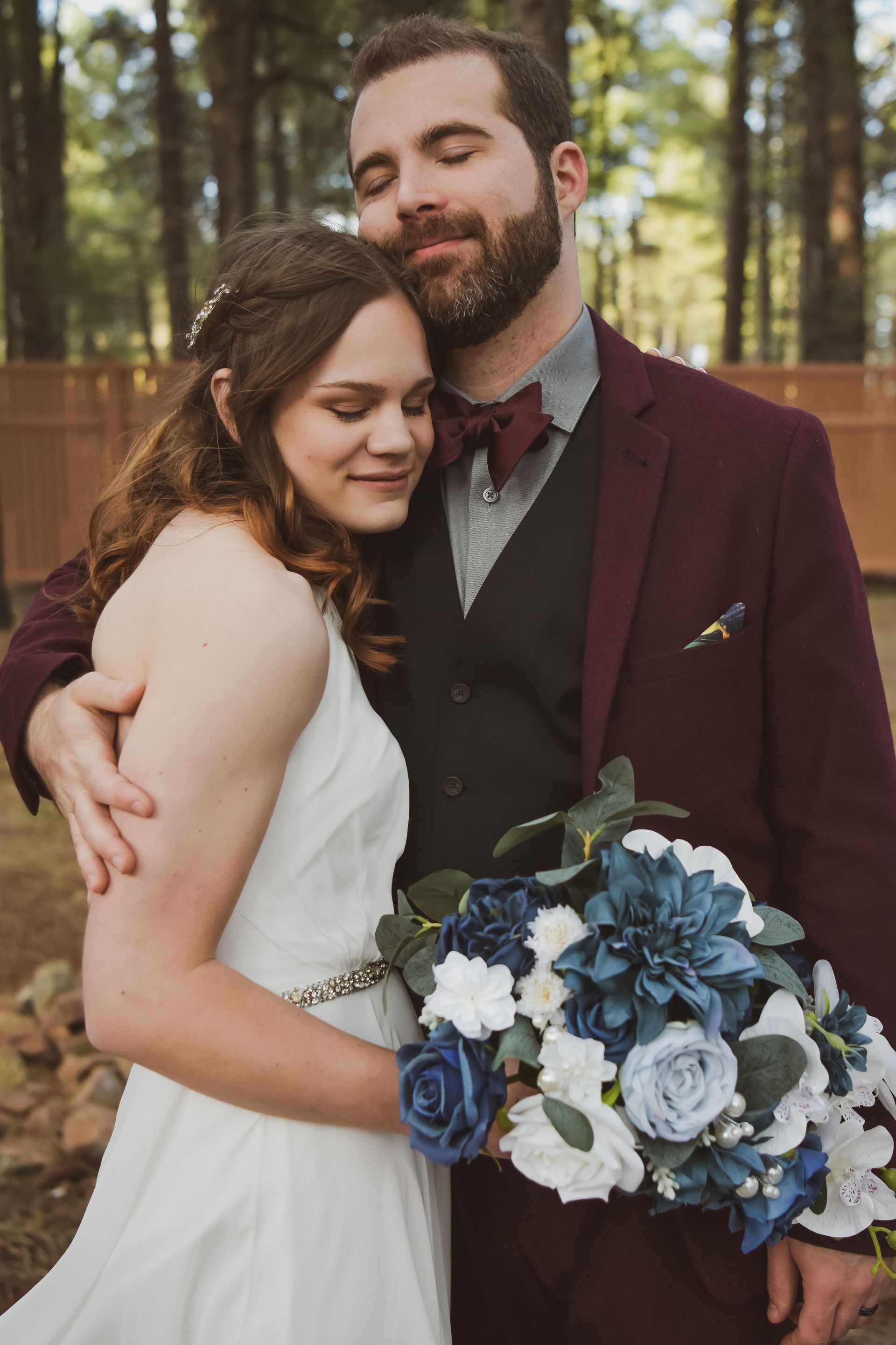 A bride and groom are posing for a picture while the bride is holding a bouquet of blue and white flowers.