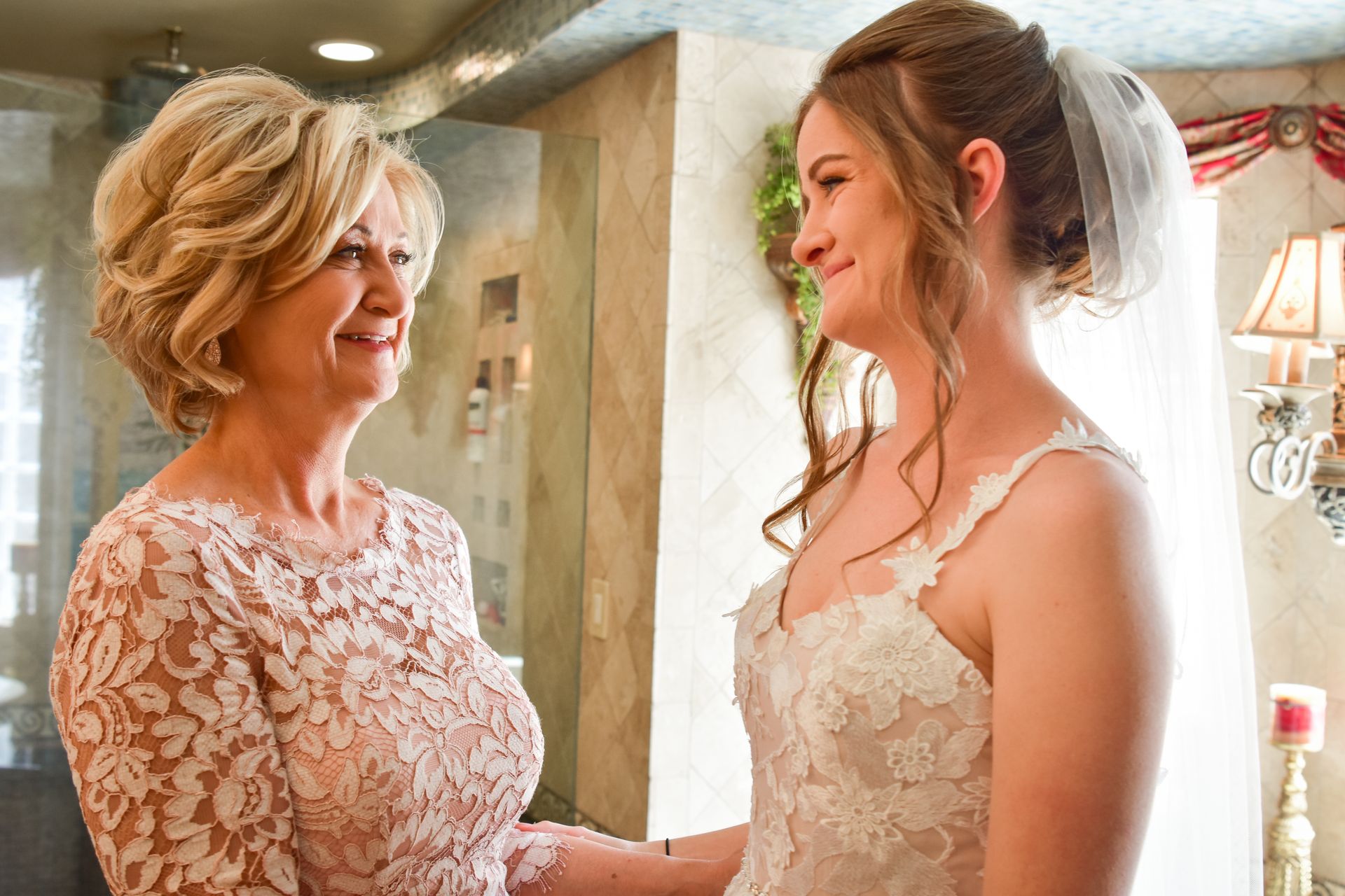 A bride and her mother are holding hands in a bathroom.