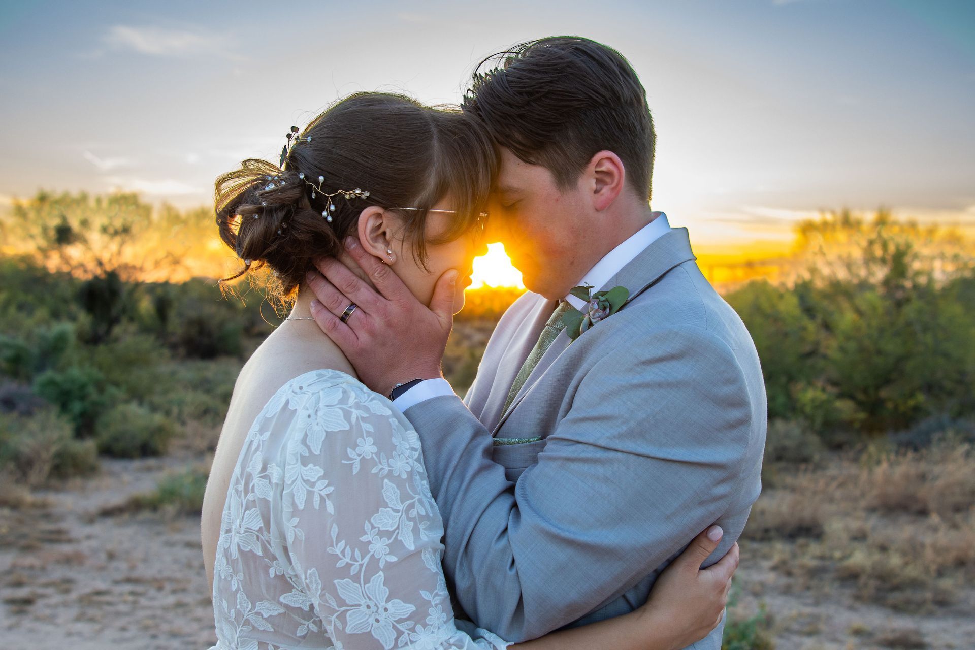 A bride and groom are kissing in front of a sunset.