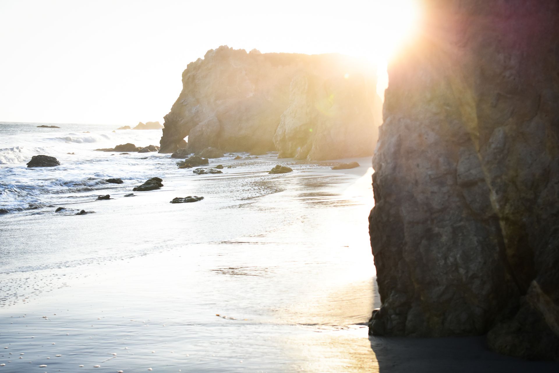 The sun is shining through the rocks on the beach