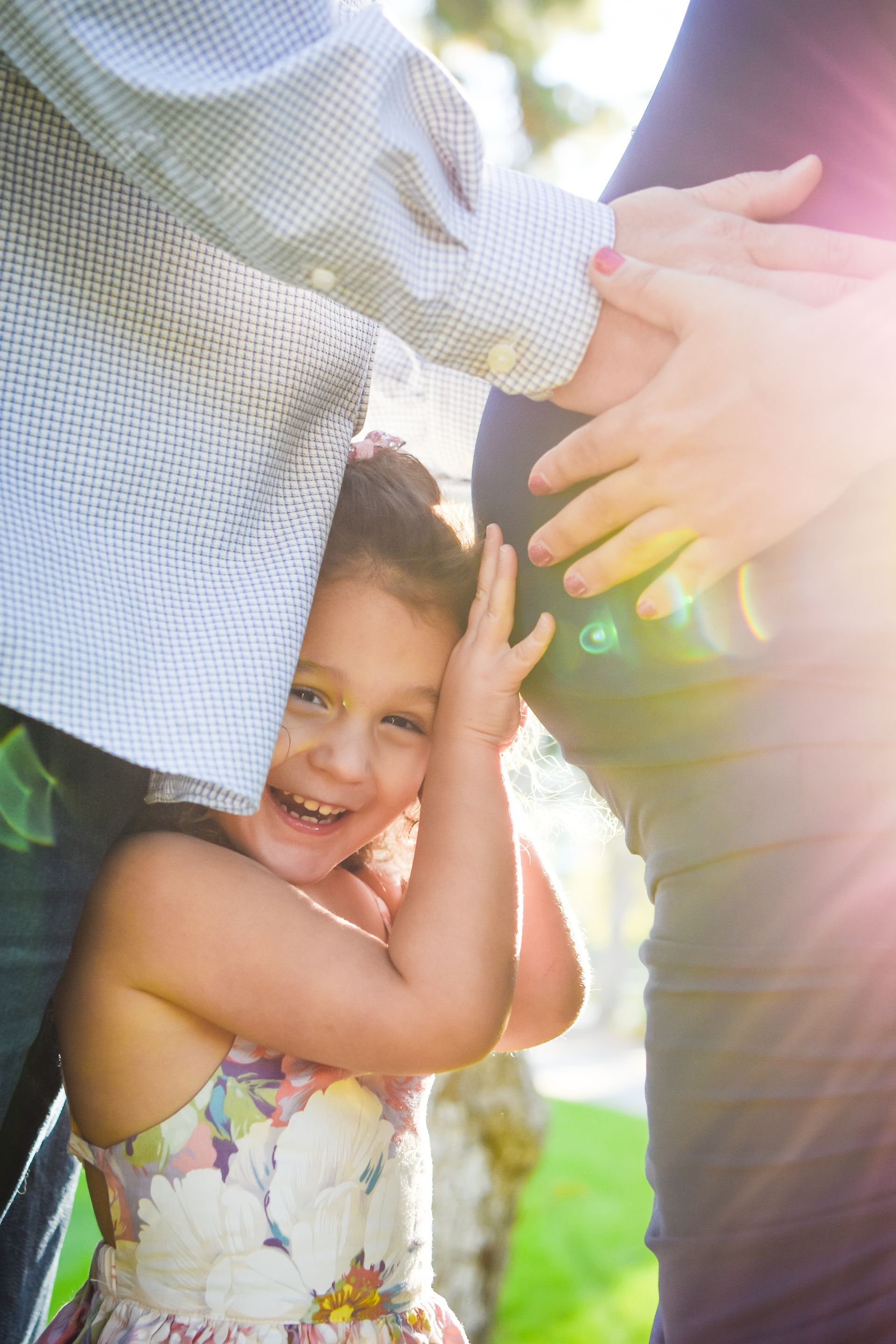 A little girl is hugging a pregnant woman 's belly.