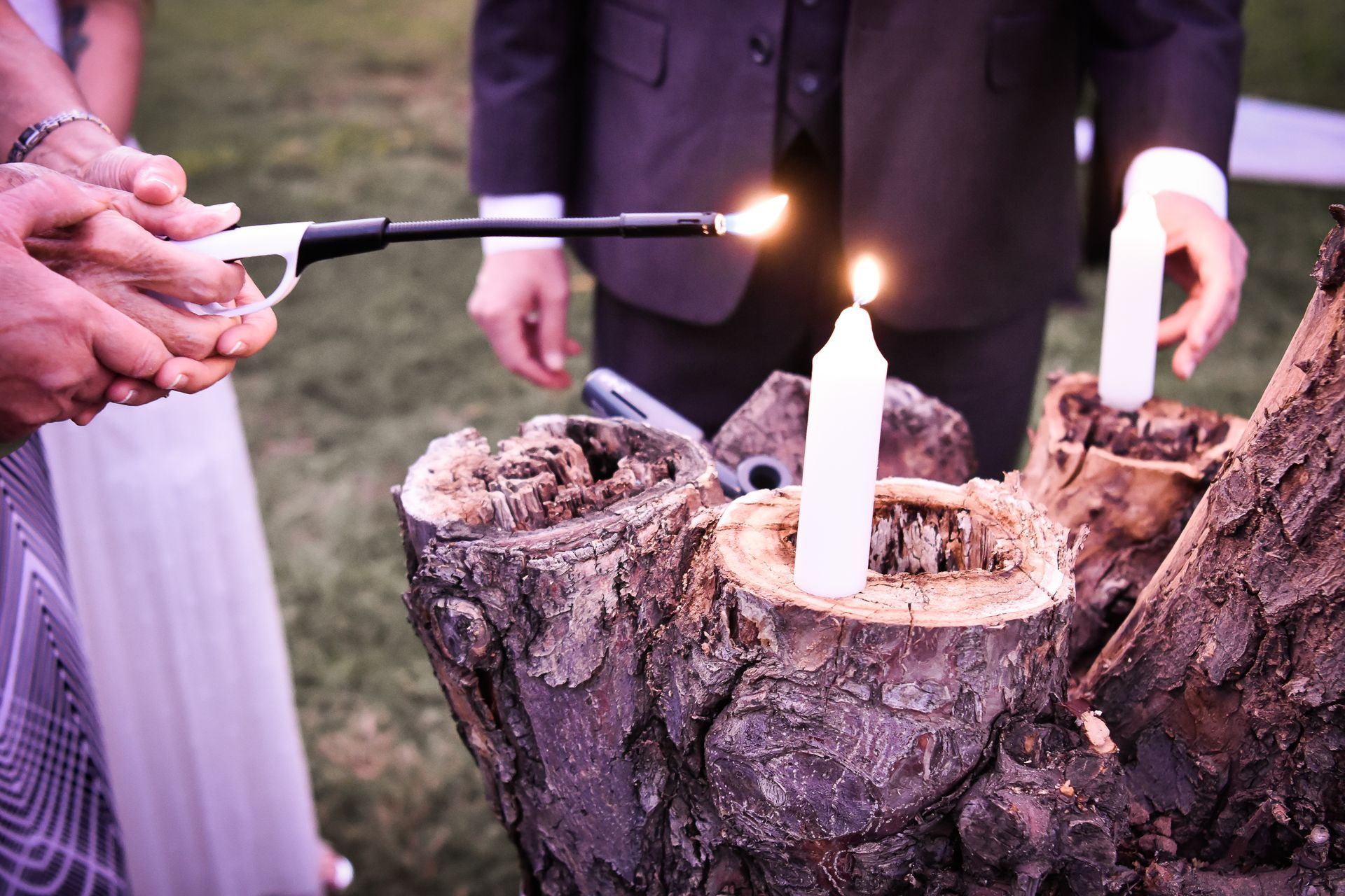 A group of people are lighting candles in tree stumps.