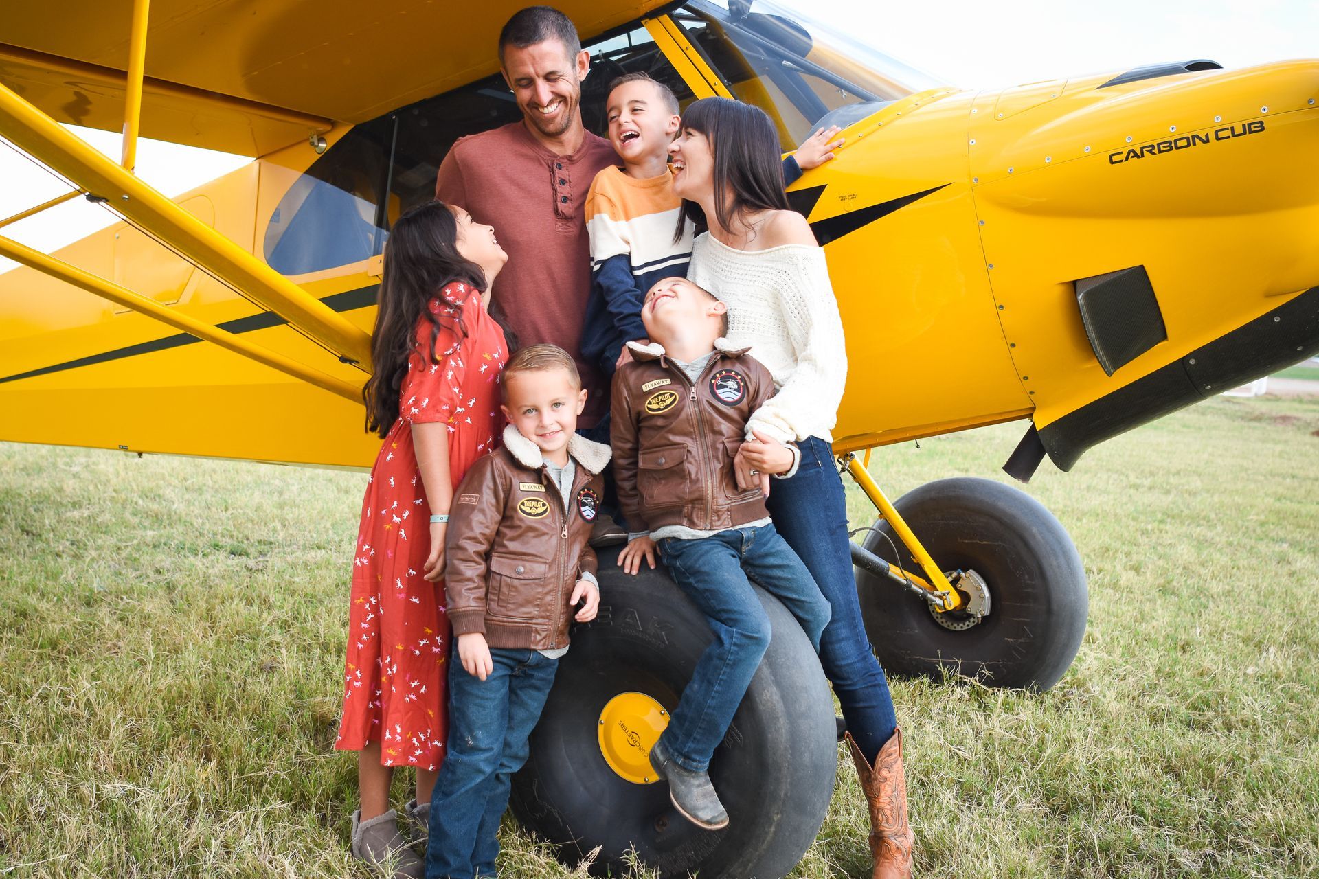 A family is posing for a picture in front of a yellow plane.