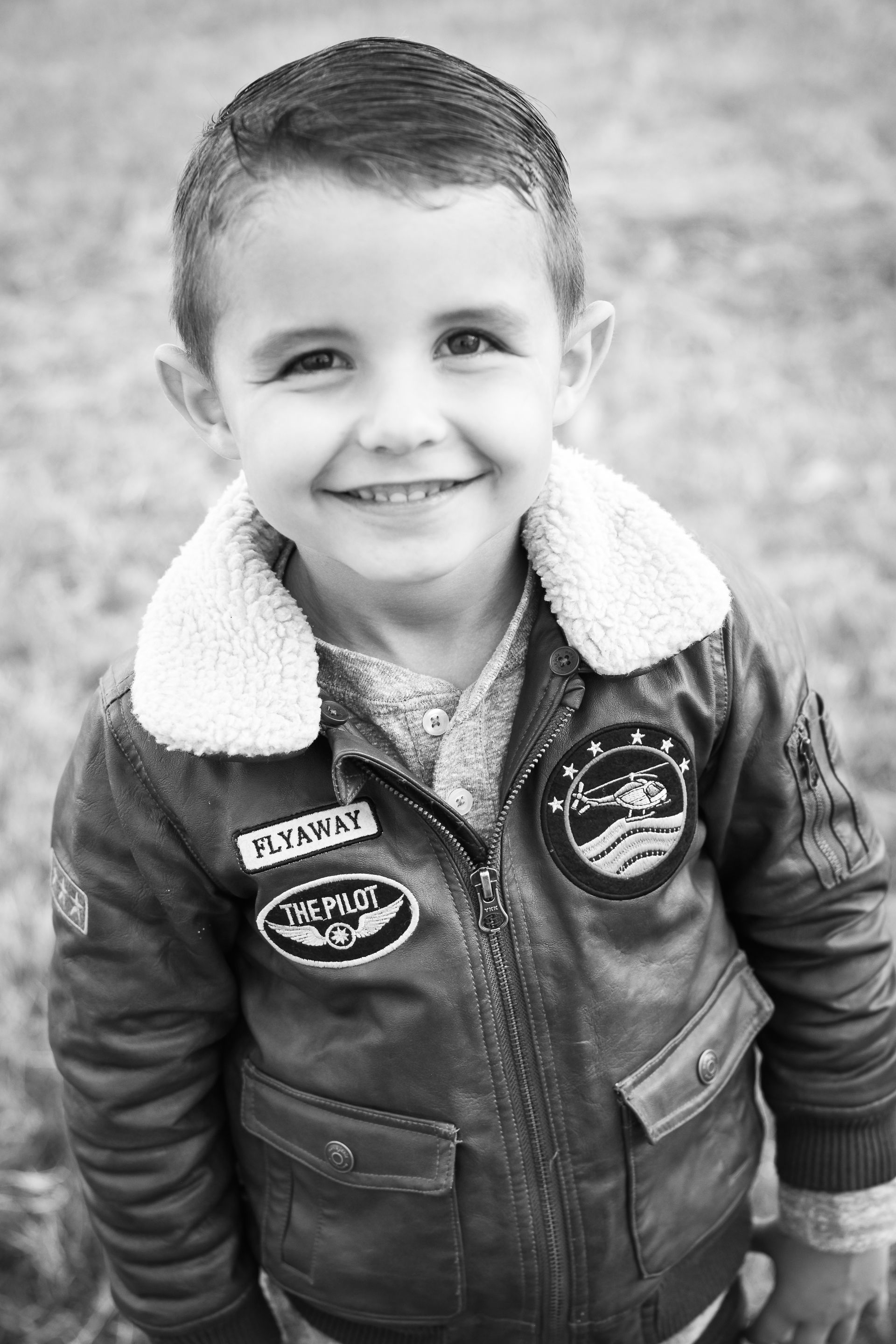 A black and white photo of a young boy wearing a leather jacket and smiling.