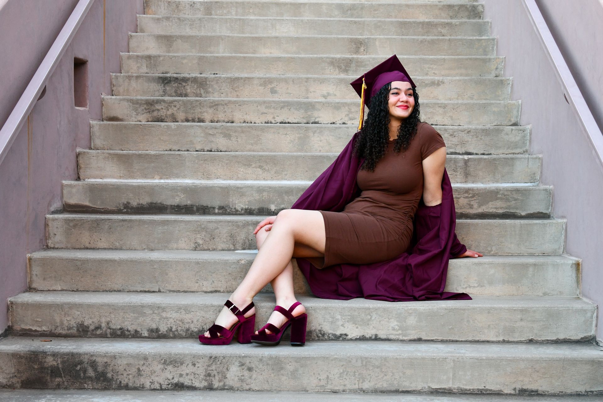 A woman in a graduation cap and gown is sitting on a set of stairs.