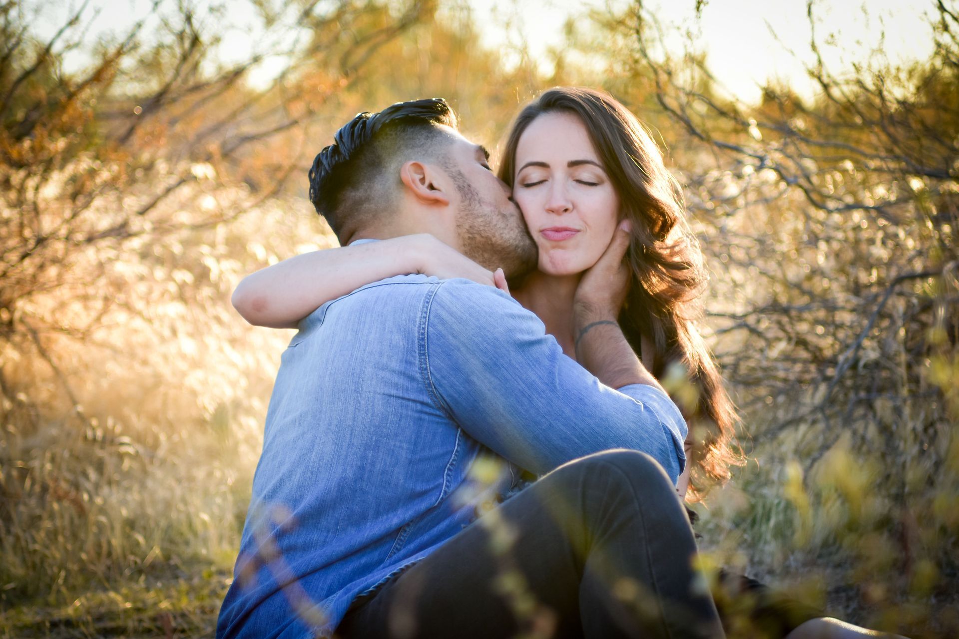 A man is kissing a woman on the cheek in a field.