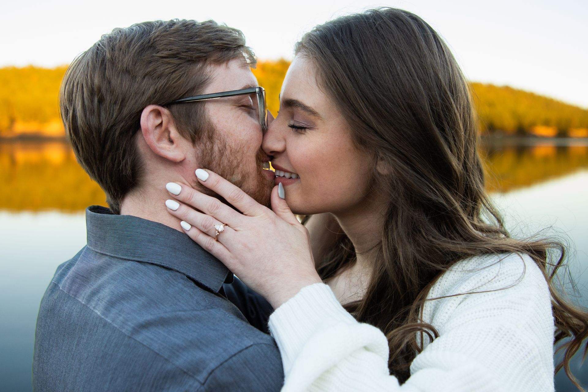 A man and a woman are kissing in front of a lake.