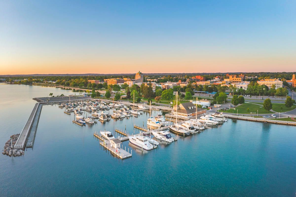 Harbor with boats docked, pier, and buildings on the shoreline at sunset.
