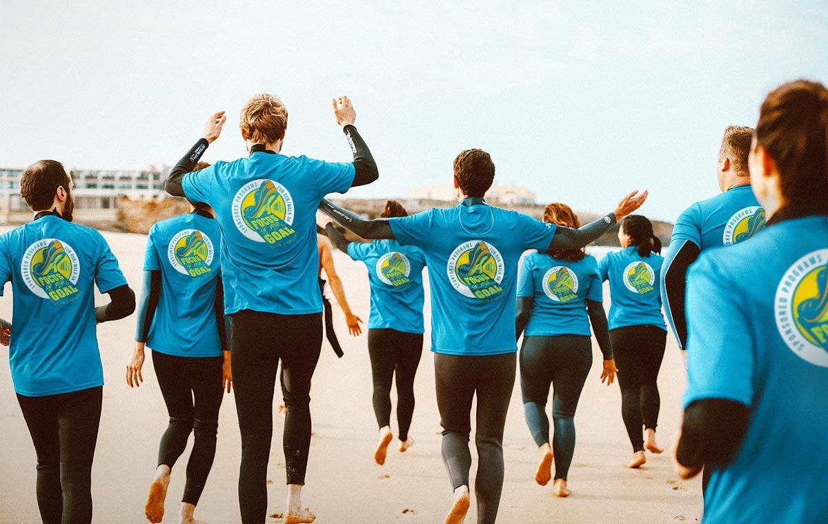 A group of people in blue shirts with a logo, walking on a beach towards the ocean.