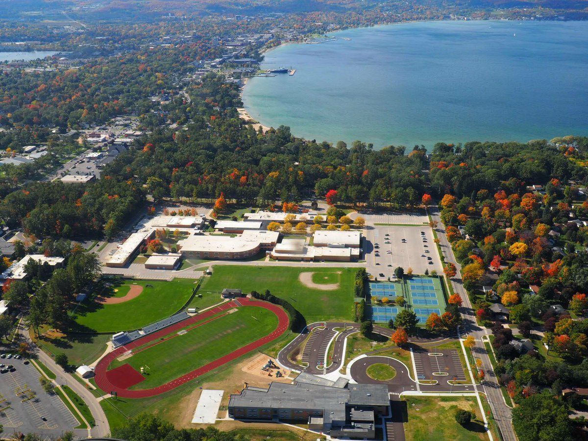 Aerial view of school complex with athletic fields, surrounded by trees and a lake.
