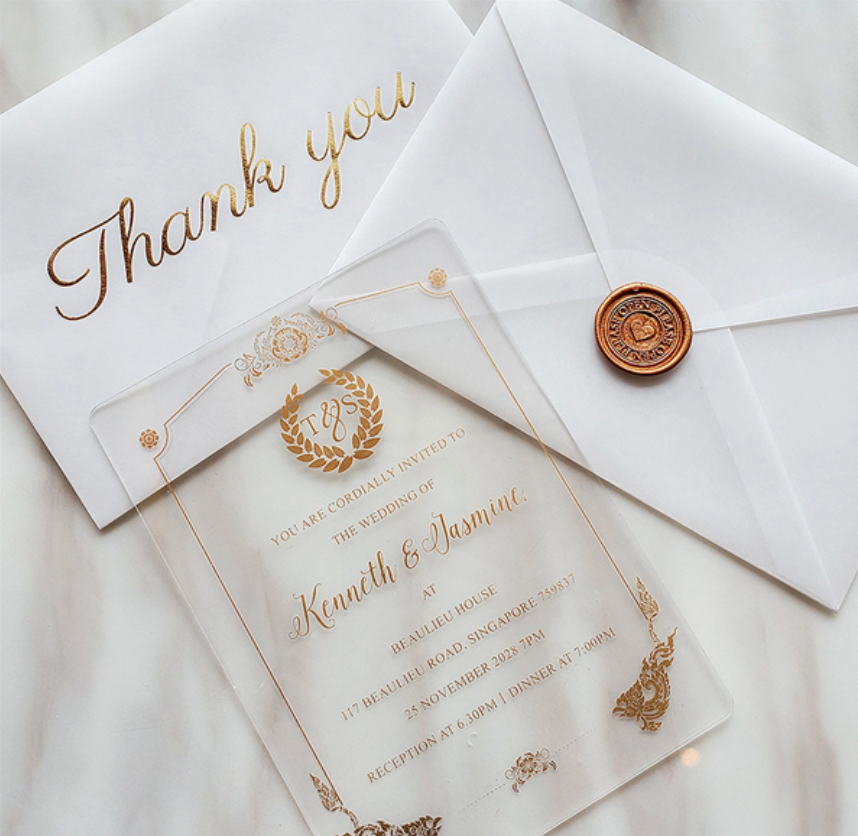 Wedding invitation suite: clear acrylic invite with gold lettering, white envelopes, wax seal, and a 