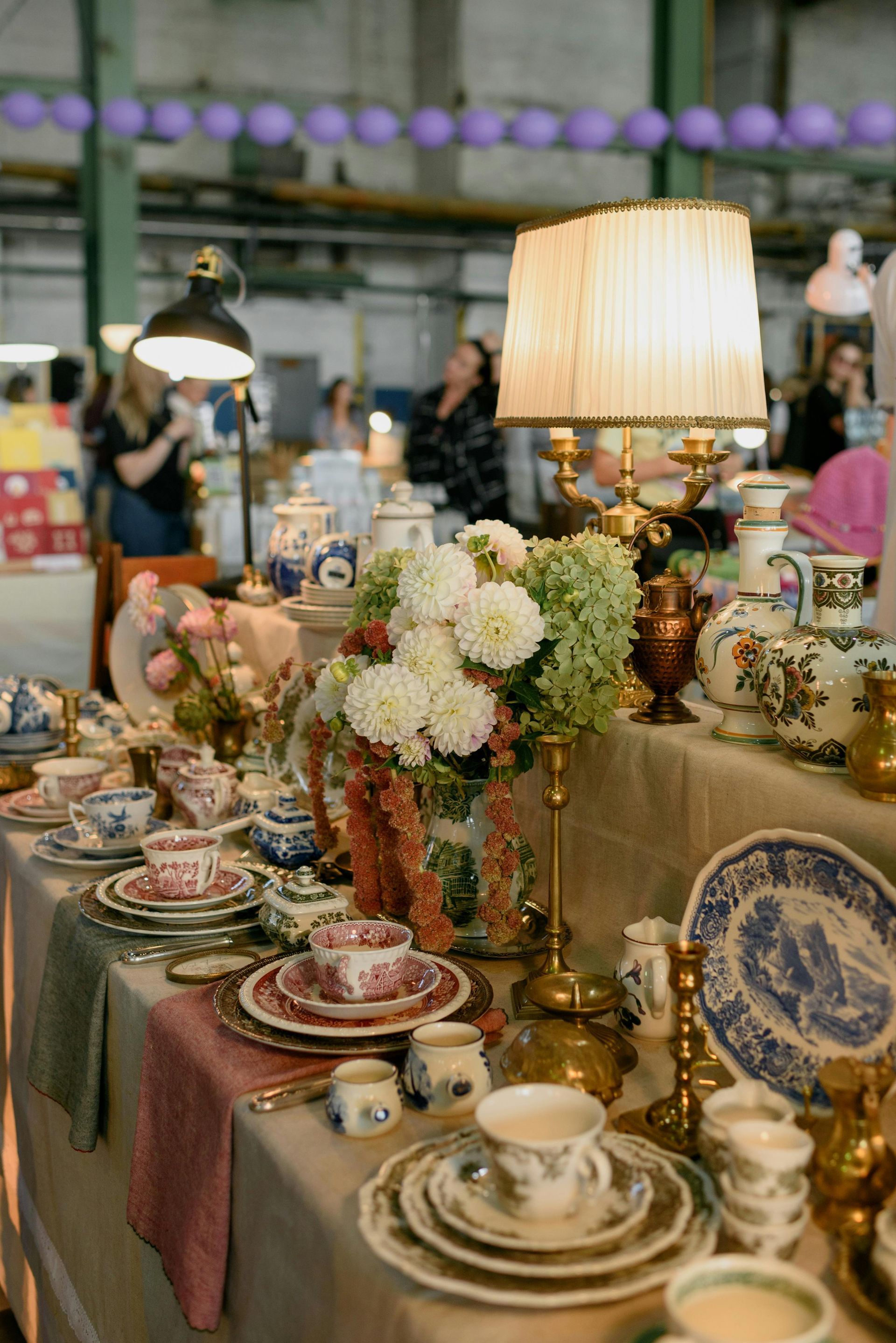 Table display with antique china, flowers, and a lamp in a vintage market.