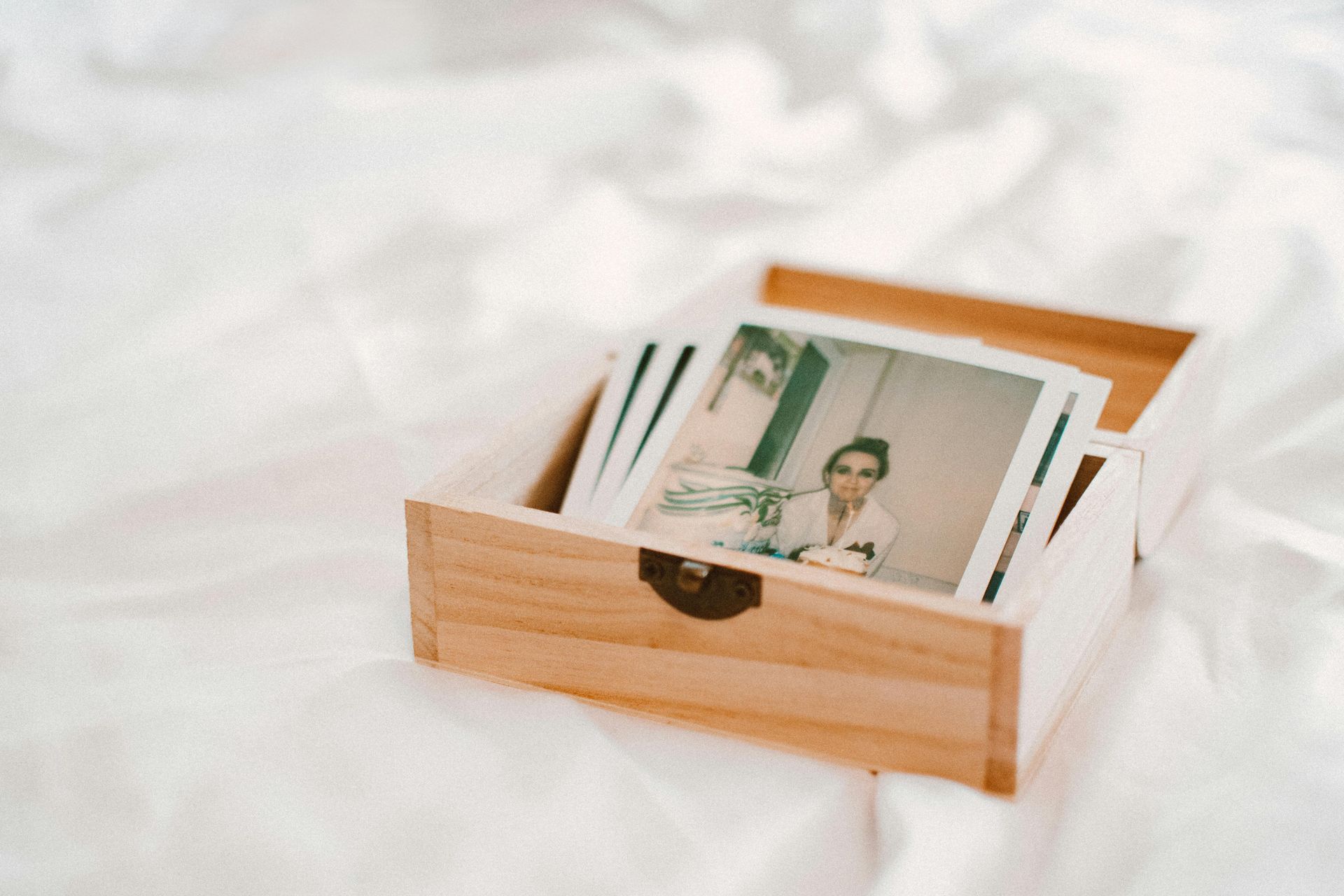 Wooden box with polaroid photos on a white bed. Box is open, showing a stack of photos.