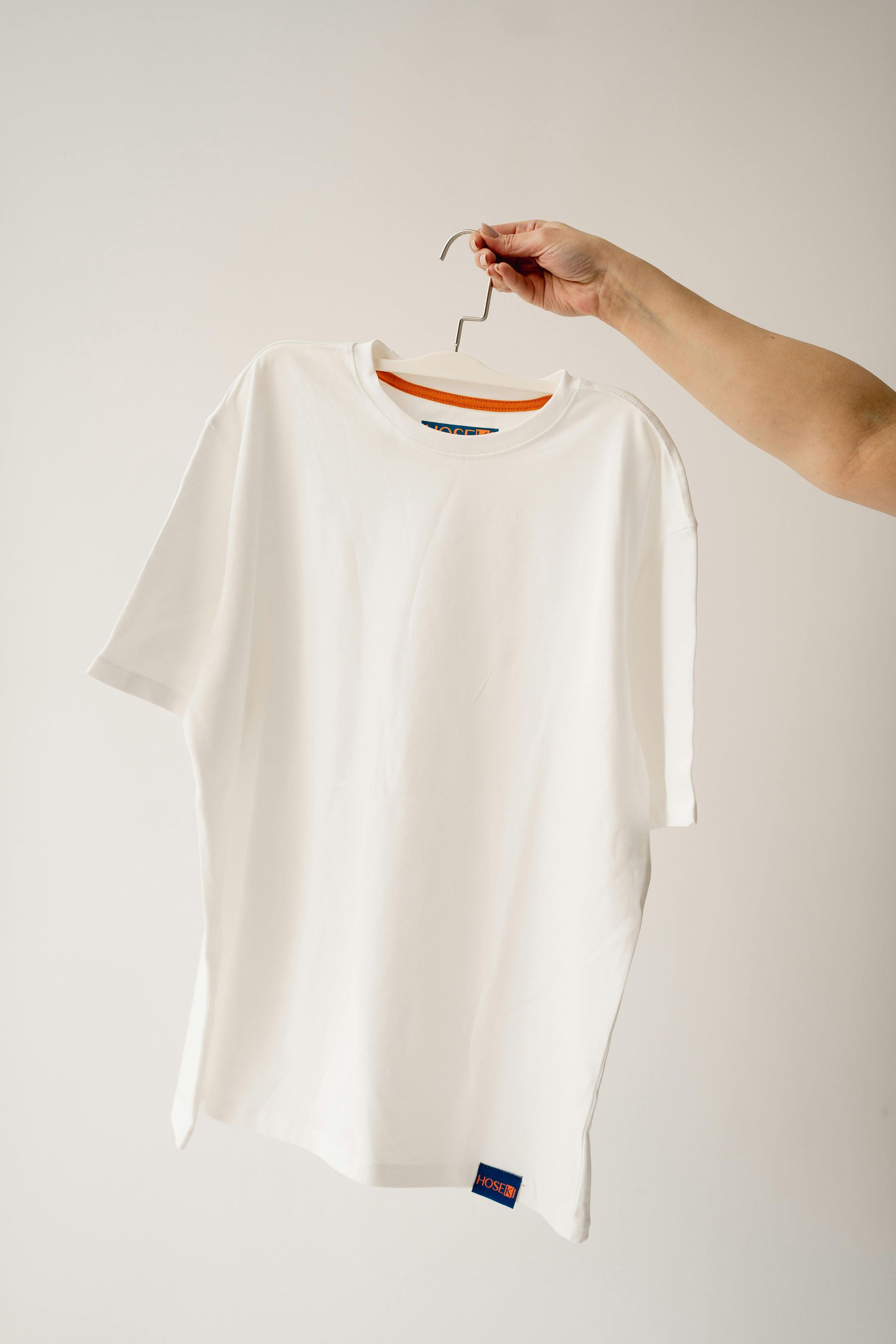 A hand holding a white t-shirt on a hanger against a white background.