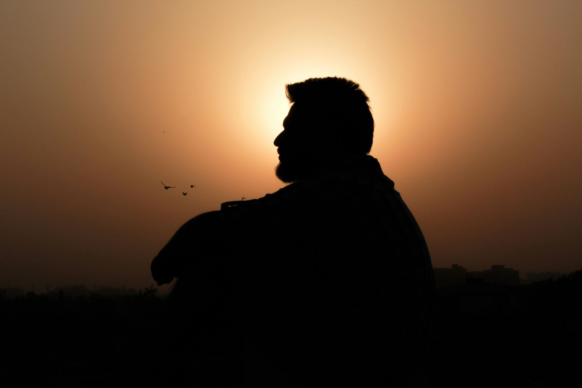 Silhouette of a person seated, facing right, against the bright sunset.