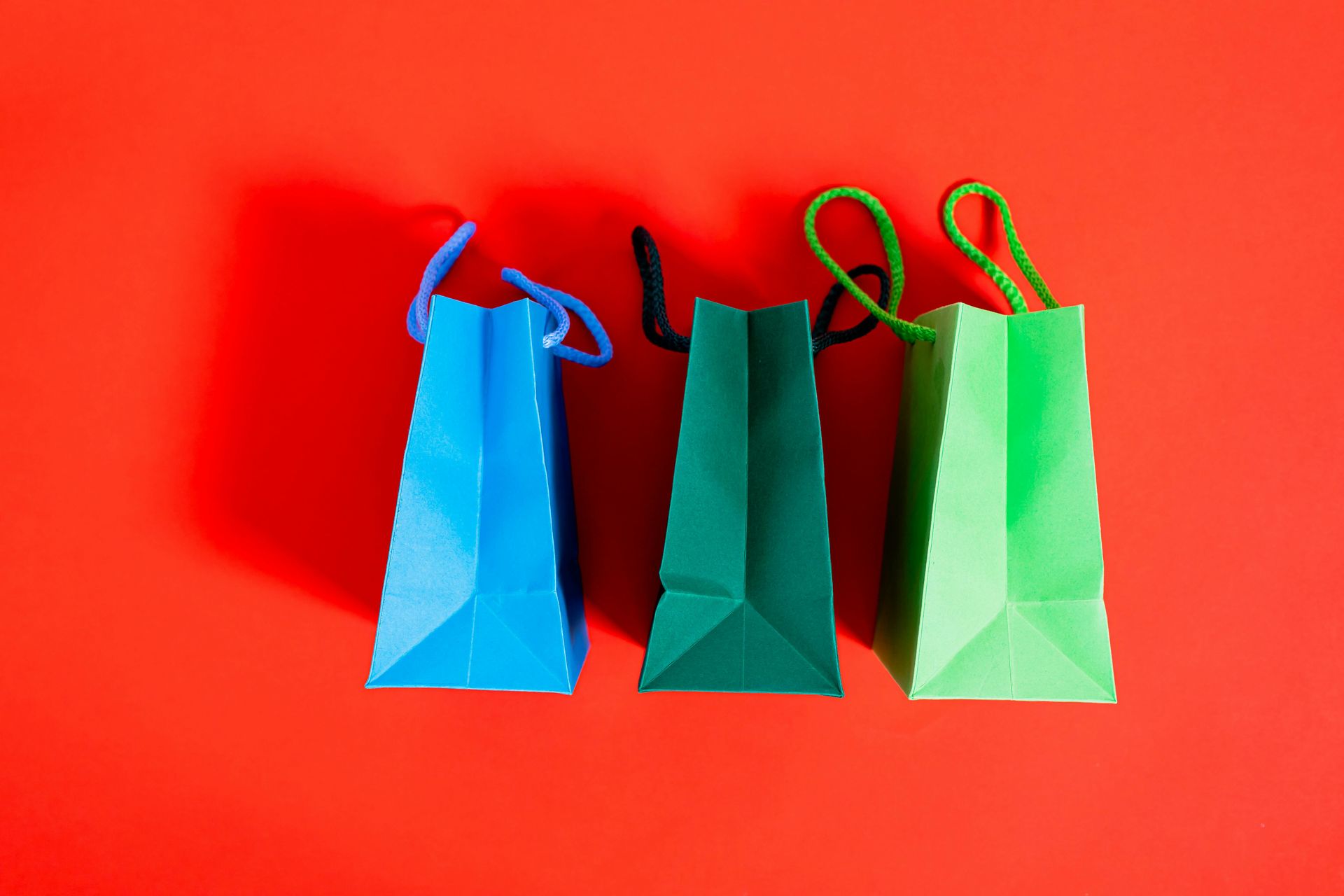 Three colorful gift bags with blue, green, and light green on a red background.