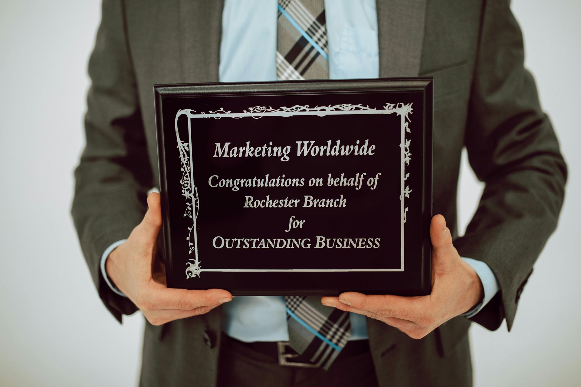 Man in suit holding an award plaque. The plaque reads: 