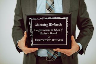 Man in suit holding an award plaque. The plaque reads: