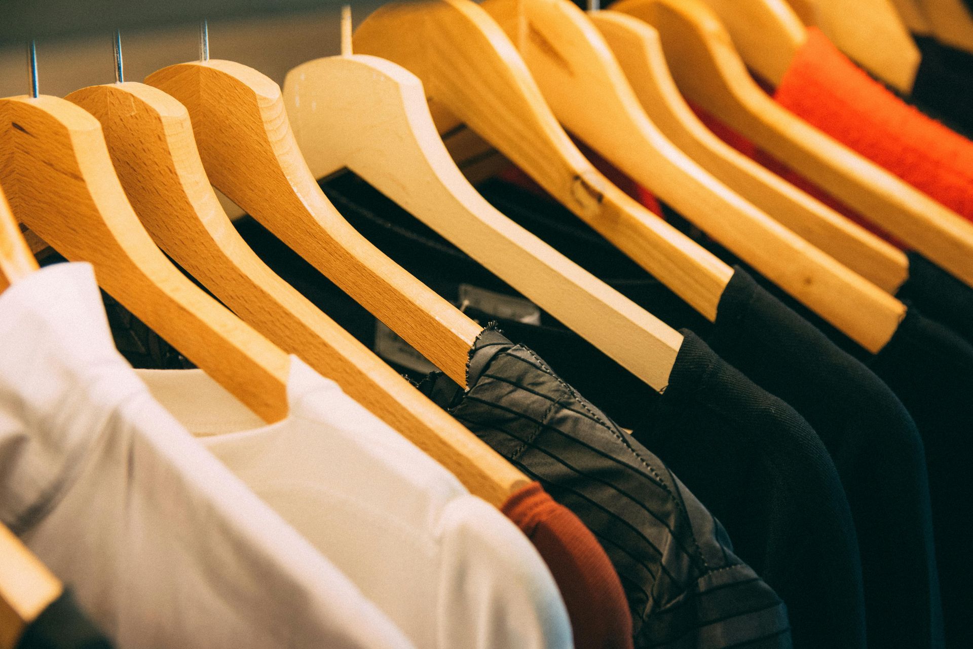 Clothes hanging on wooden hangers, various colors: white, black, orange and red.