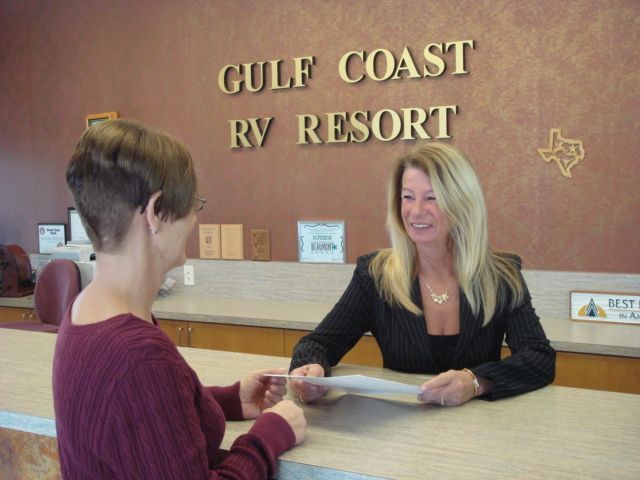 Woman at Gulf Coast RV Resort reception desk handing paperwork to another woman.