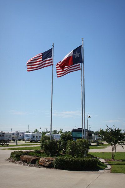 American and Texas flags flying on poles, with a recreational vehicle park in the background.