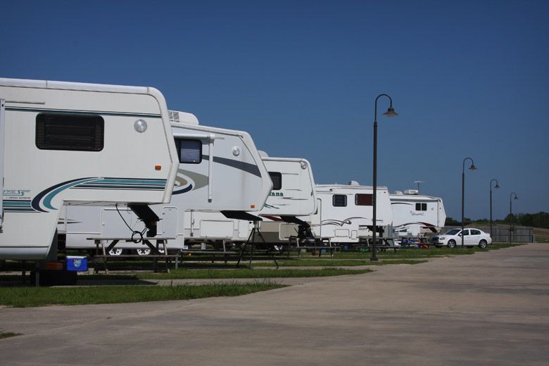 RV campground with multiple white RVs parked along a concrete lane under a blue sky.
