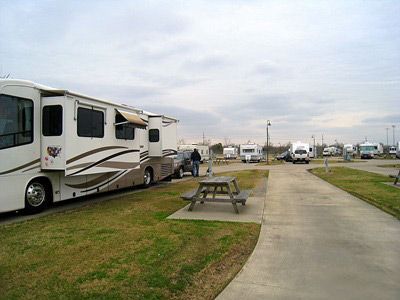 RV park with several recreational vehicles parked on paved sites. Cloudy sky overhead.