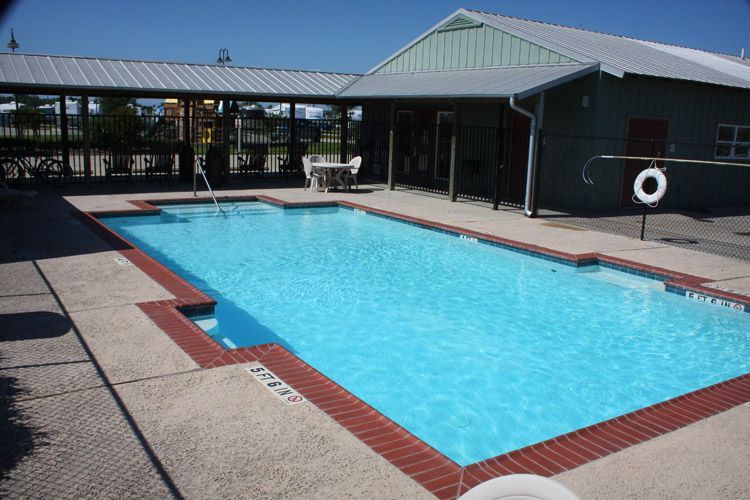 Swimming pool with turquoise water, brick border, and adjacent building with a metal roof.
