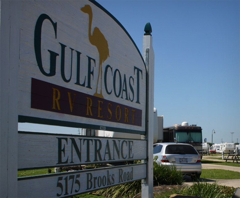 Sign for Gulf Coast RV Resort, white with green and maroon text, heron logo, Brooks Road address.