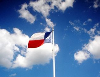 Texas flag waving against a bright blue sky with fluffy white clouds.
