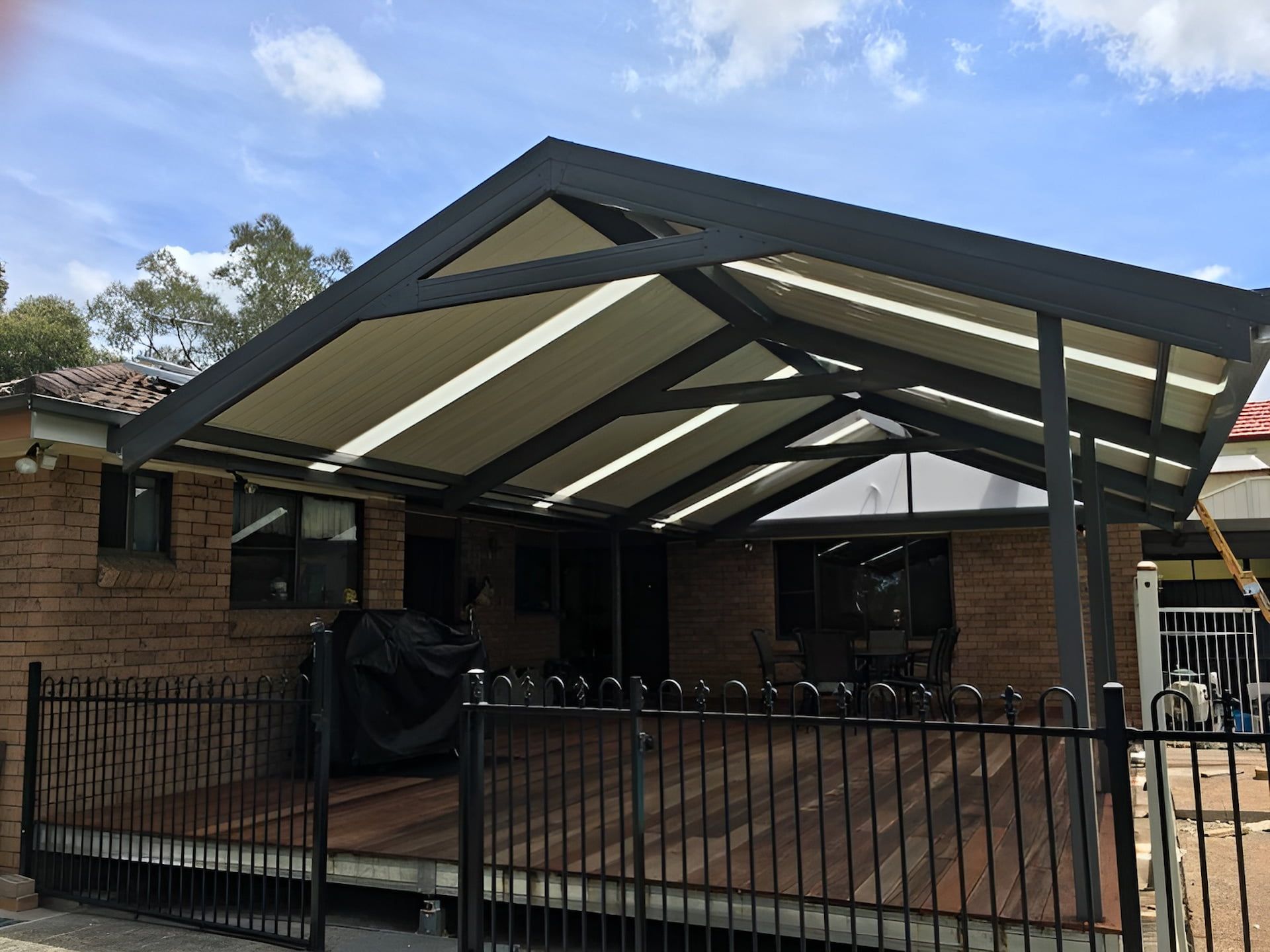 A Black Framed Patio Cover Over a Wooden Deck, Attached to A Brick Home — Hunter Home Services in Cessnock, NSW