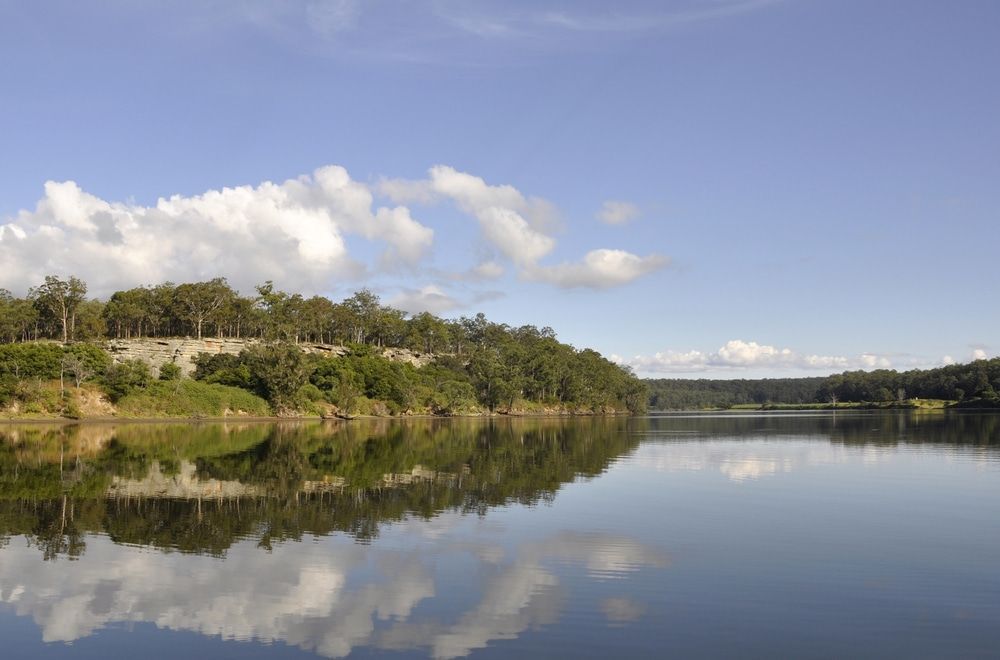 A Large Body of Water with Trees on The Shore and Clouds Reflected in The Water — Leisure Coast Powder Coaters in Nowra, NSW