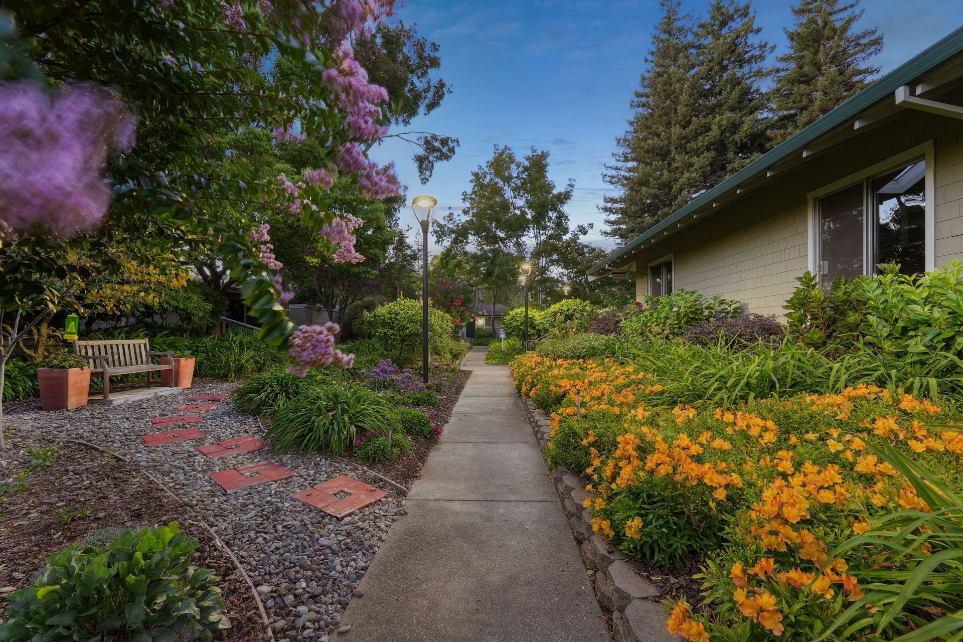 A walkway leading to a house surrounded by flowers and trees