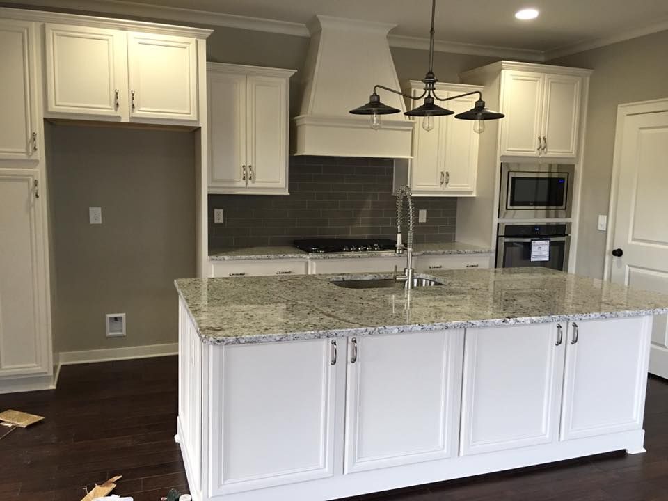 White kitchen with granite countertops, stainless steel appliances, and a brown leather sofa in the foreground.