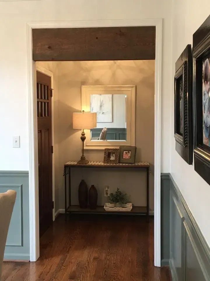 Hallway view:  A dark wood-trimmed doorway leads to a foyer with a console table, mirror, and lamp.