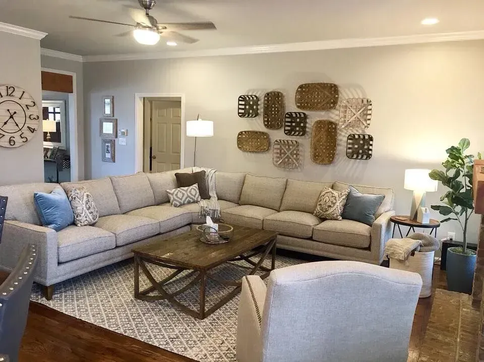 Cozy living room with a light-colored sectional sofa, textured wall baskets, and a patterned rug.