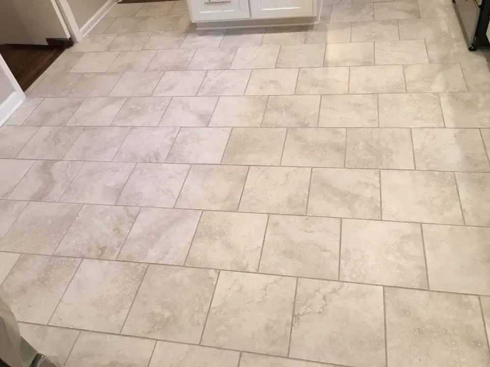 Beige rectangular tiles laid in a staggered pattern cover a floor, possibly in a kitchen or entryway.
