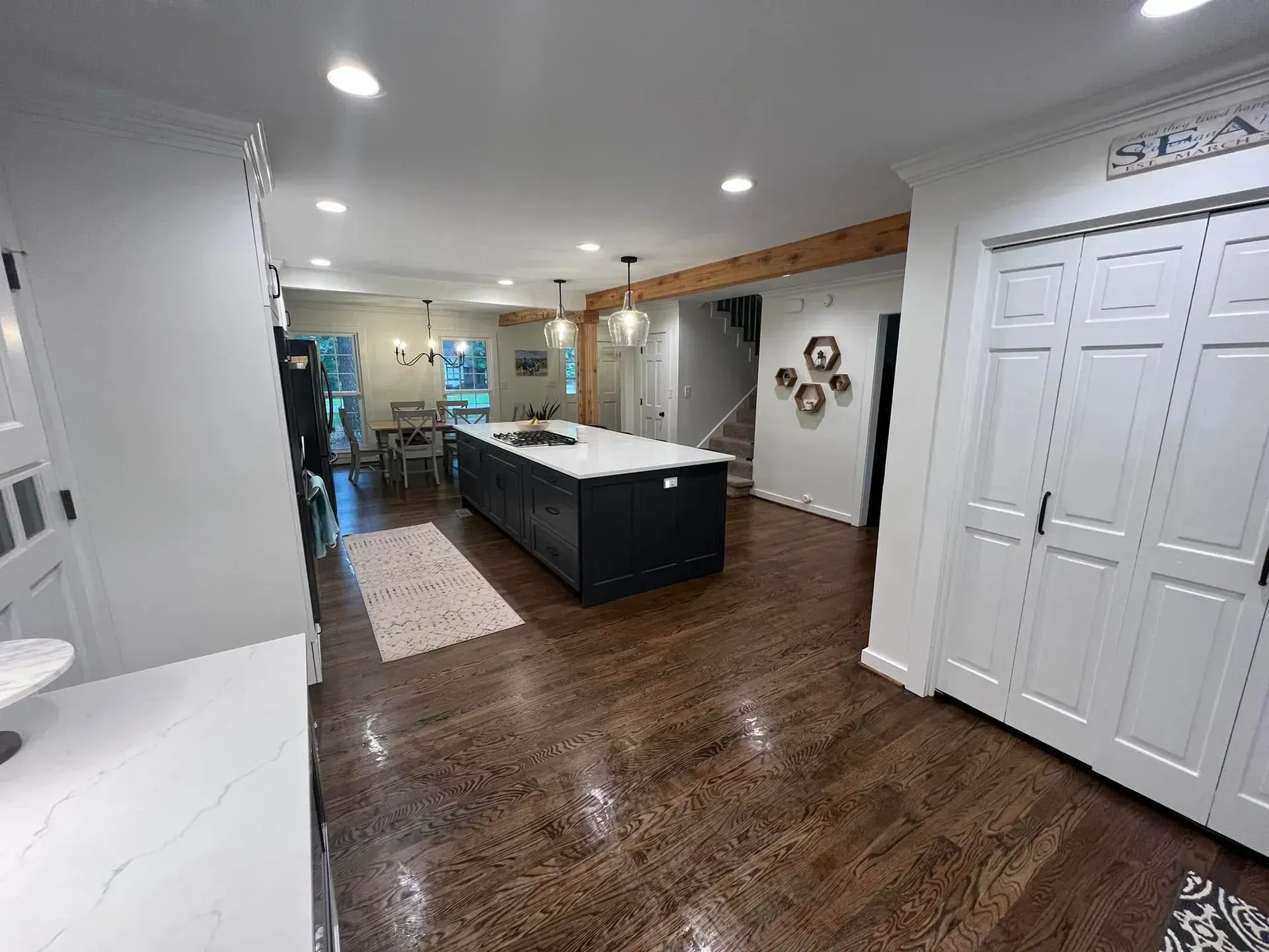 Spacious kitchen with dark wood floors, white cabinetry, and a large navy island. Dining area visible in the background.