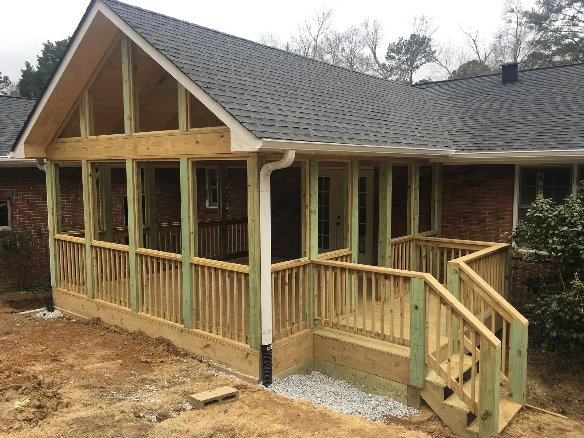 Newly constructed screened-in porch with wooden railings and stairs attached to a brick house. Green lumber is visible.