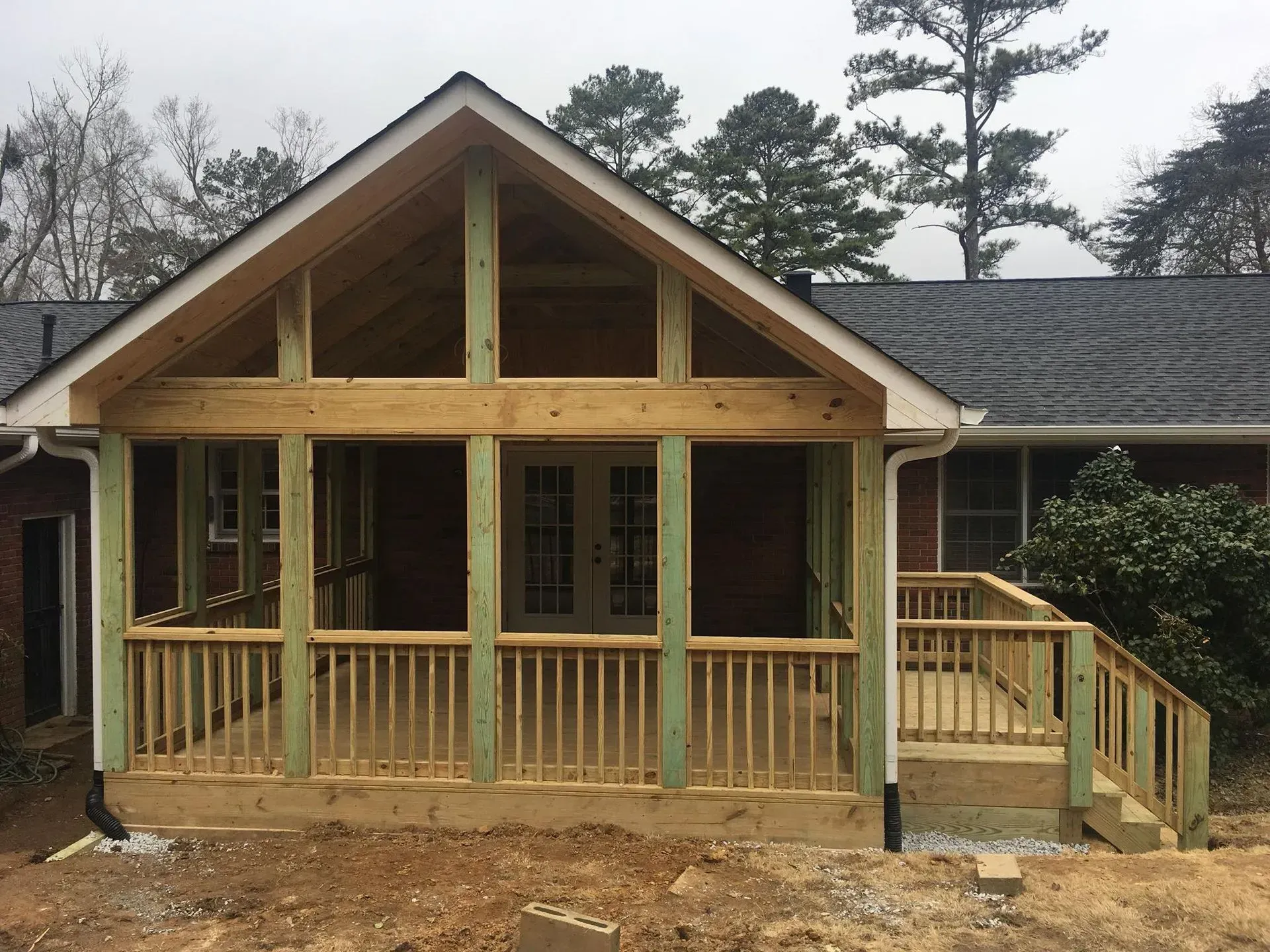 Screened-in porch under construction. Green-treated lumber frames the structure; natural wood railing.