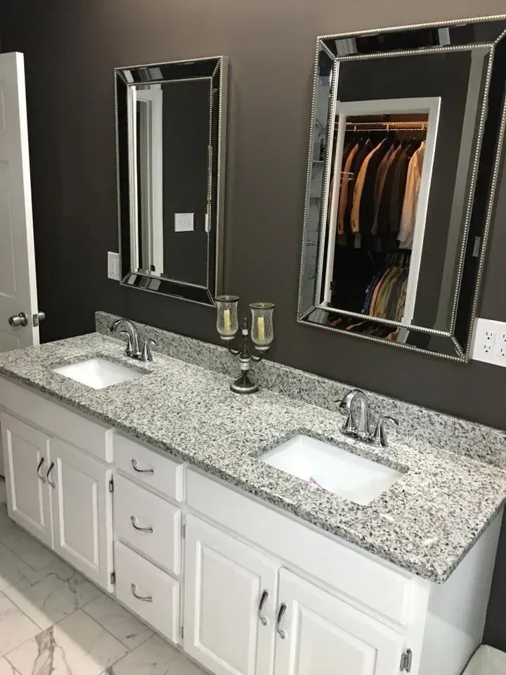Bathroom with white double vanity, granite countertop, two mirrors, and a dark gray wall. The right mirror reflects a closet.