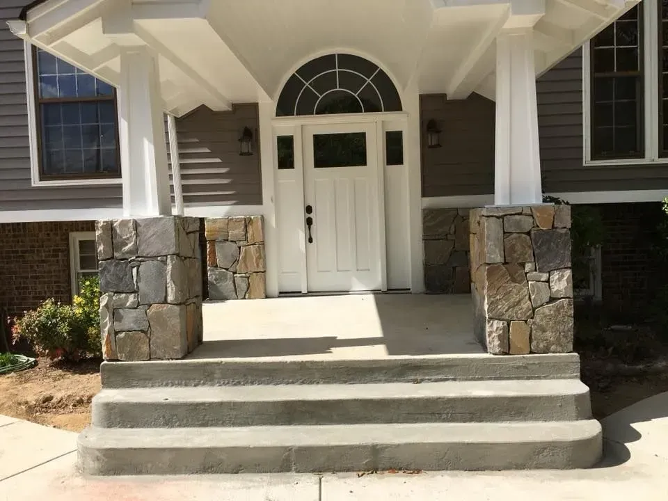Front entrance of a house with stone columns, steps, and a white door under an arched window.