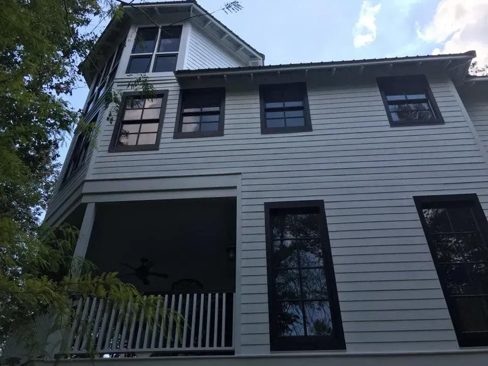 A three-story, light-colored house with dark window frames and a porch. The sky is visible above.