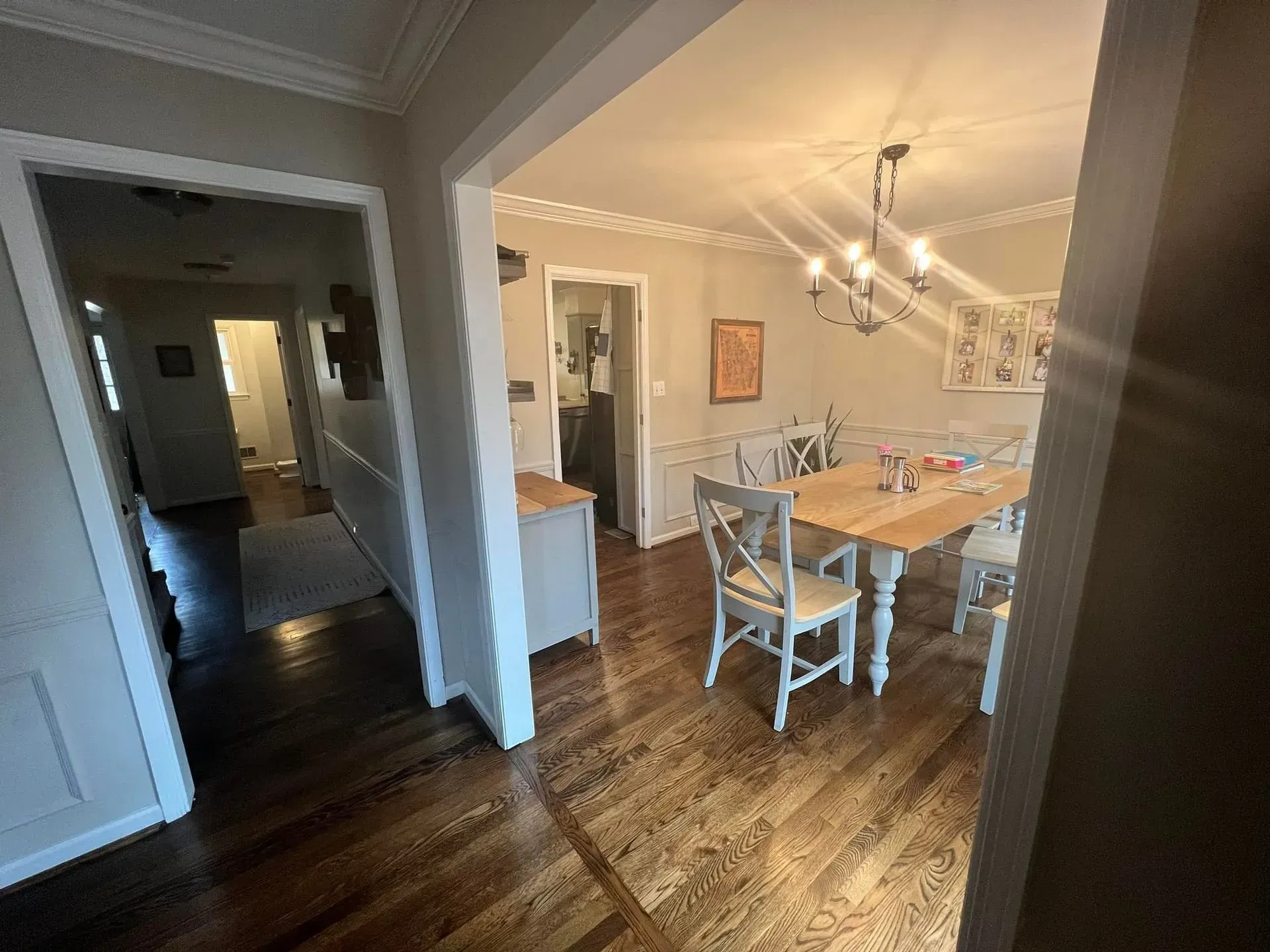 A view from a doorway shows a dining room with a table and chairs and a hallway. Dark wood floors and beige walls.