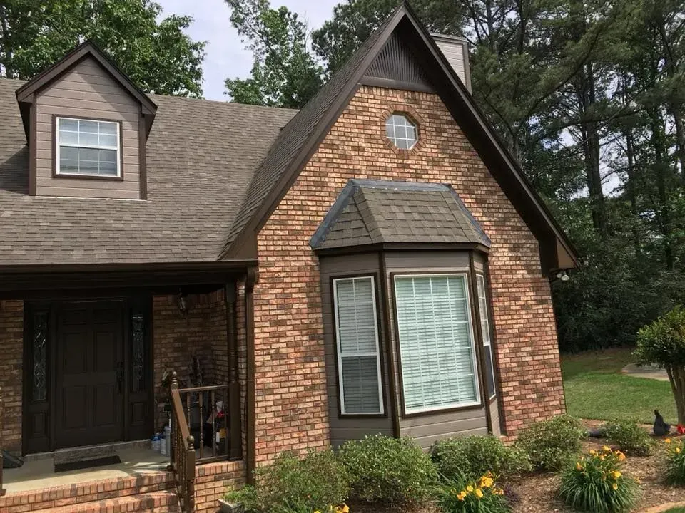 Brick house with brown trim, bay window, and a small front porch, set against a green lawn and trees.