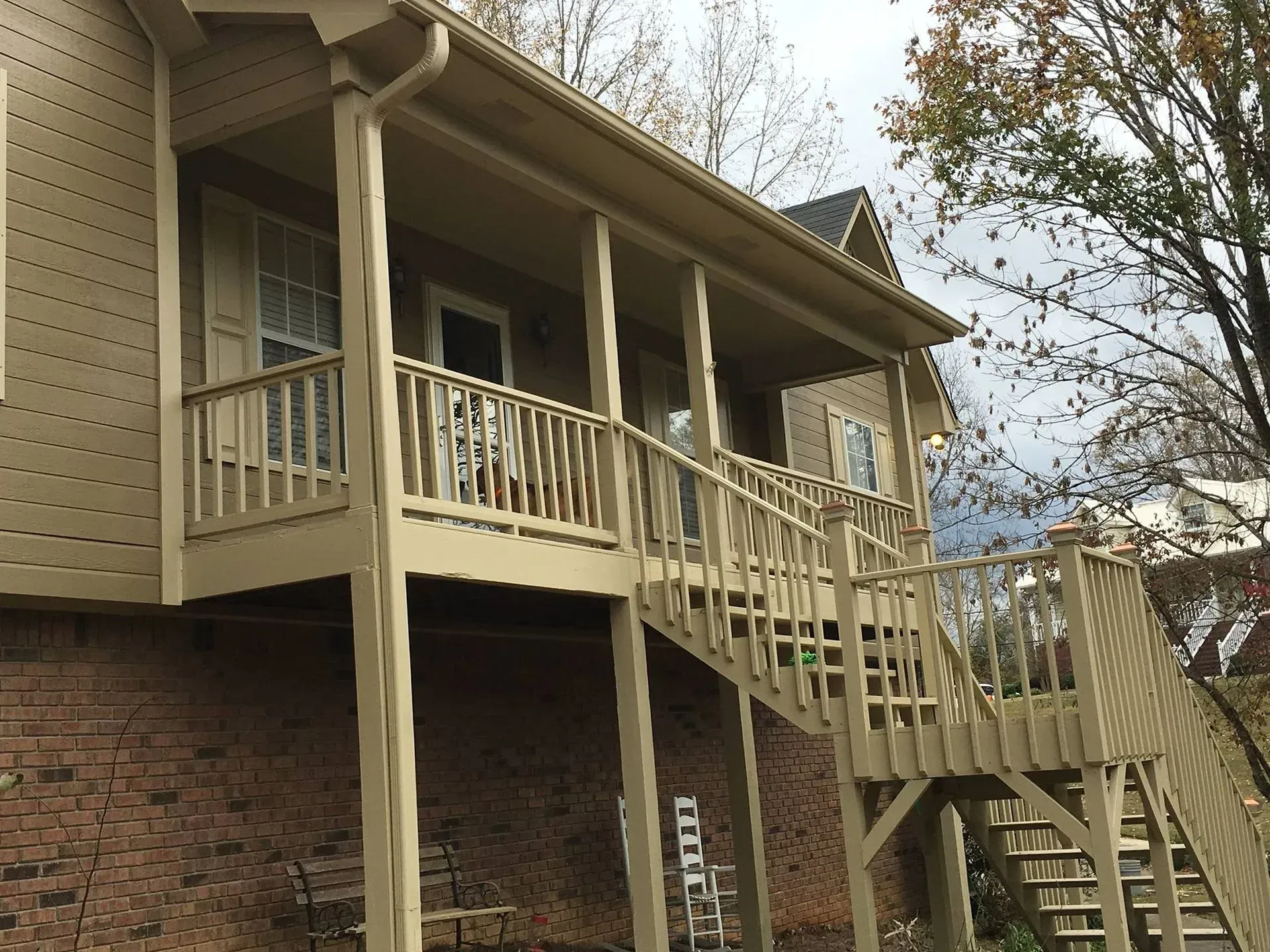 Tan wooden deck and staircase attached to a brick-walled house. The deck has a railing and supports.
